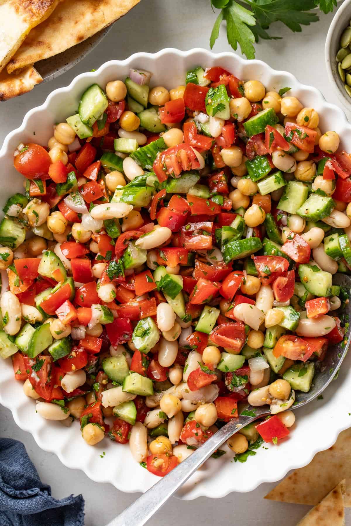 A dense bean salad mixed together in a white bowl with a spoon.