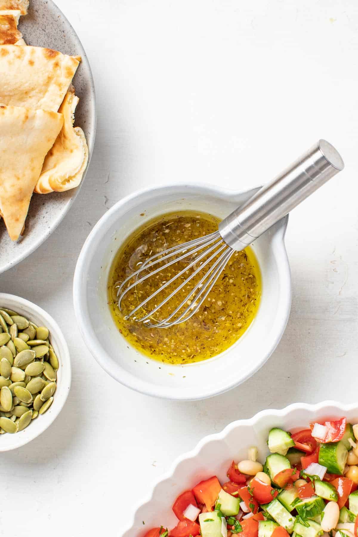 A mediterranean olive oil dressing blended together in a small white bowl with a whisk.