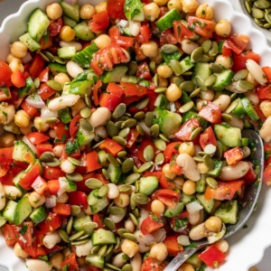 A spoon dipping into a Mediterranean dense bean salad with pumpkin seeds on top.
