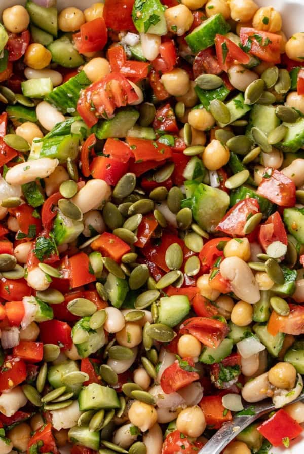 A spoon dipping into a Mediterranean dense bean salad with pumpkin seeds on top.