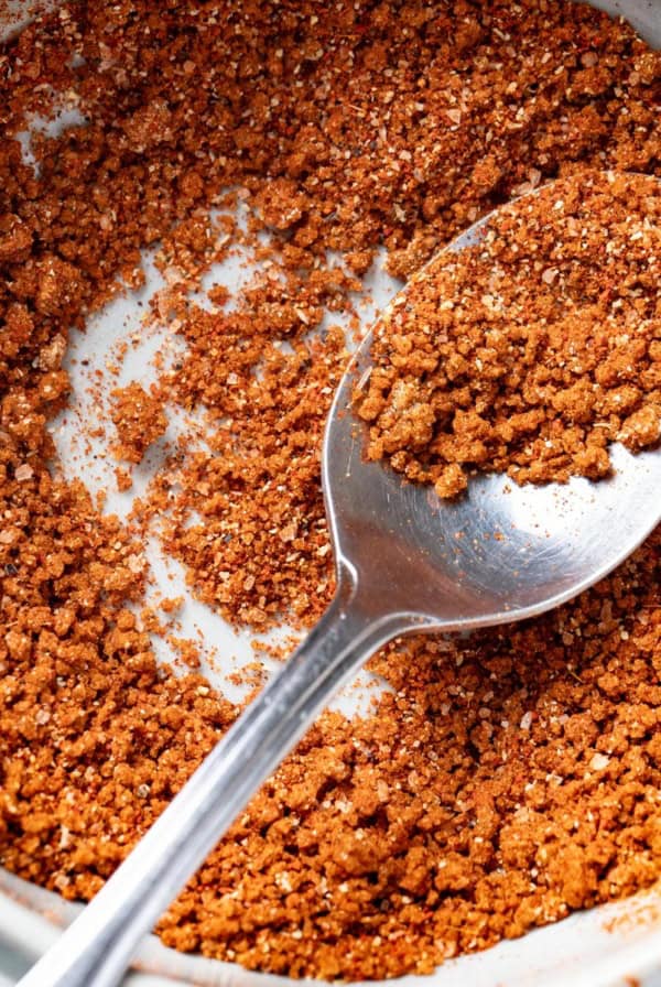 A spoon scooping into a bowl with a dry rub for ribs.