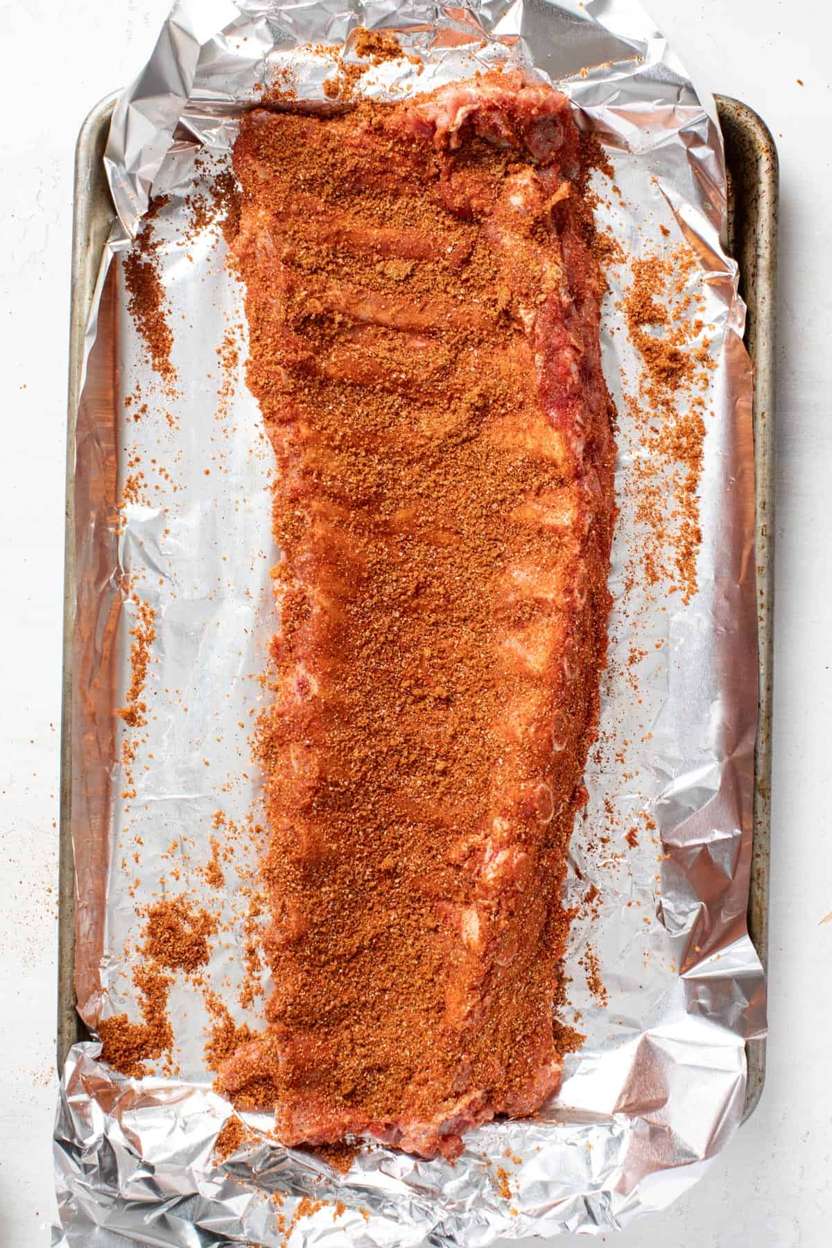 A dry rub being patted onto a rack of ribs. 
