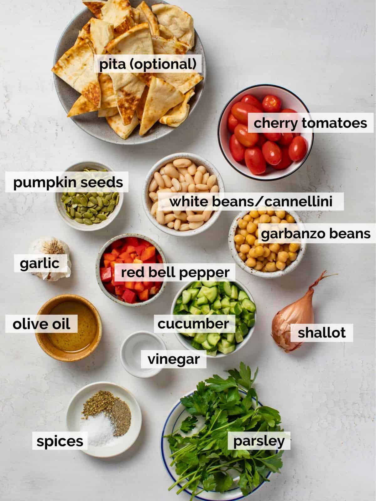 Ingredients for a Mediterranean bean salad on a white background, including cannellini beans, garbanzo beans, parsley, and olive oil.