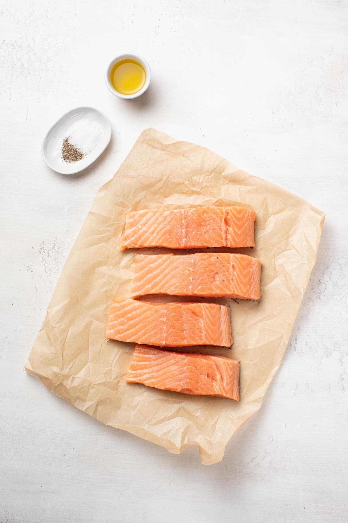 Salmon fillets, salt and pepper, and olive oil on a white background.