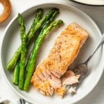 A pan seared salmon with a fork flaking pieces of it on a plate.