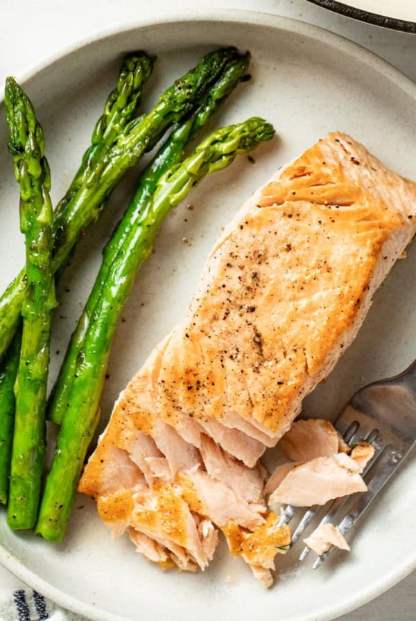 A pan seared salmon with a fork flaking pieces of it on a plate.