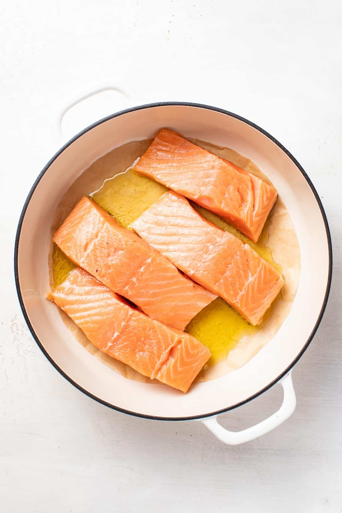 Salmon fillets in a pan with parchment topped with olive oil.