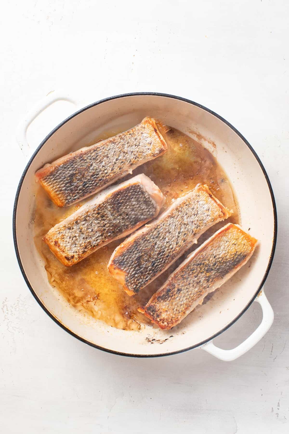 Salmon with the seared skin on top in a pan.