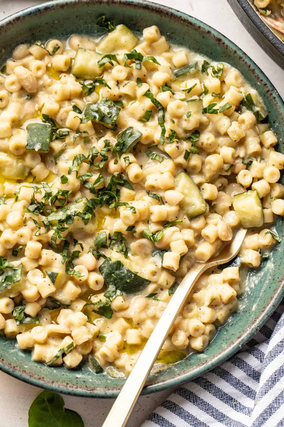 A spoon dipping into a bowl pasta with zucchini topped with chopped basil.