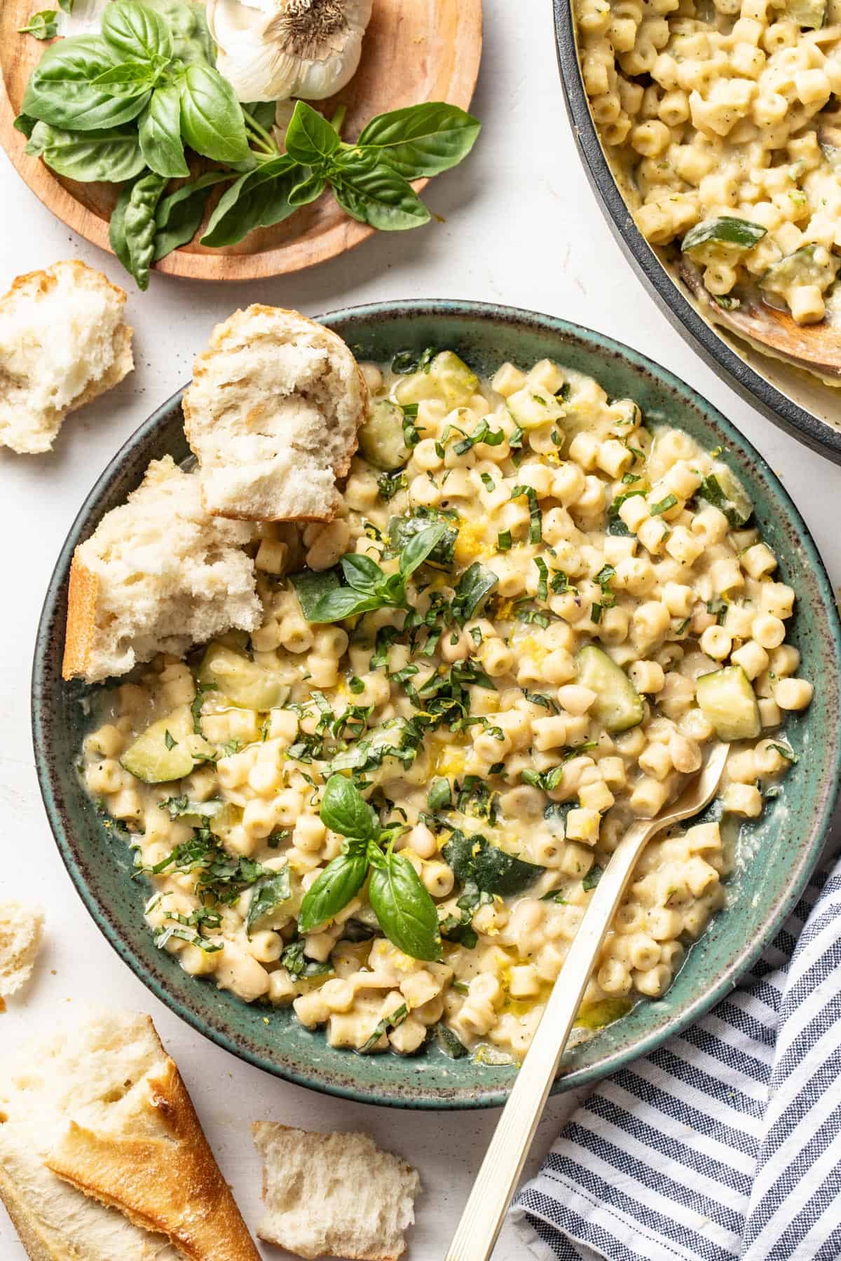 A bowl of creamy ditalini pasta with zucchini and basil next to a toasted, torn baguette.