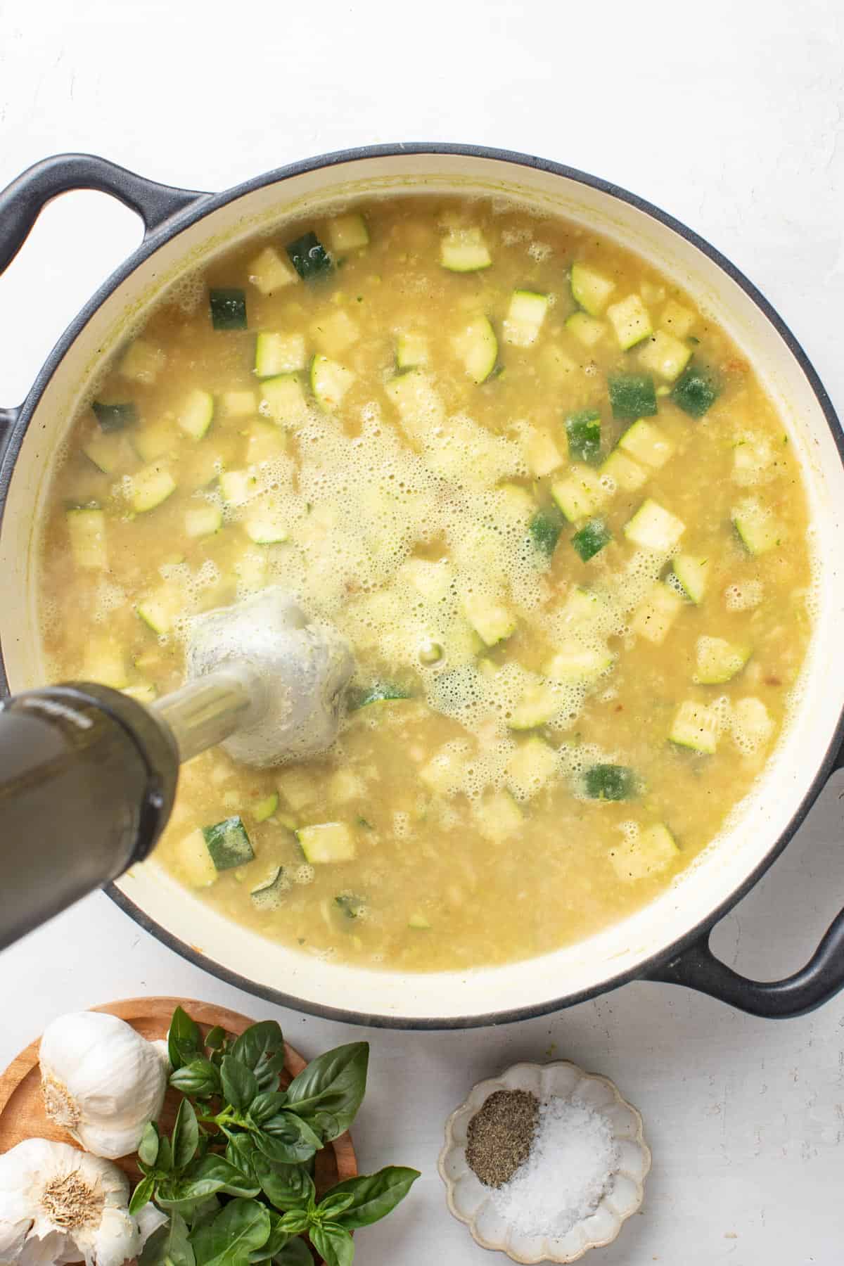 Using an immersion blender to blend the broth, beans, and zucchini together.