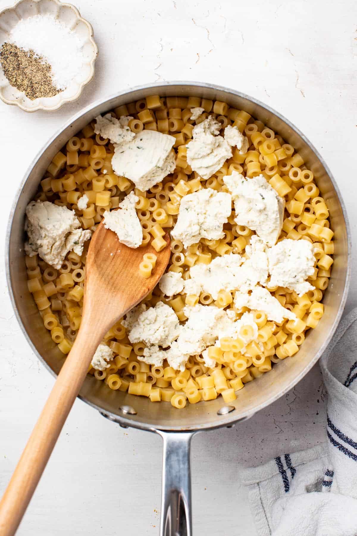 Adding Boursin cheese to the ditalini pasta saucepan.