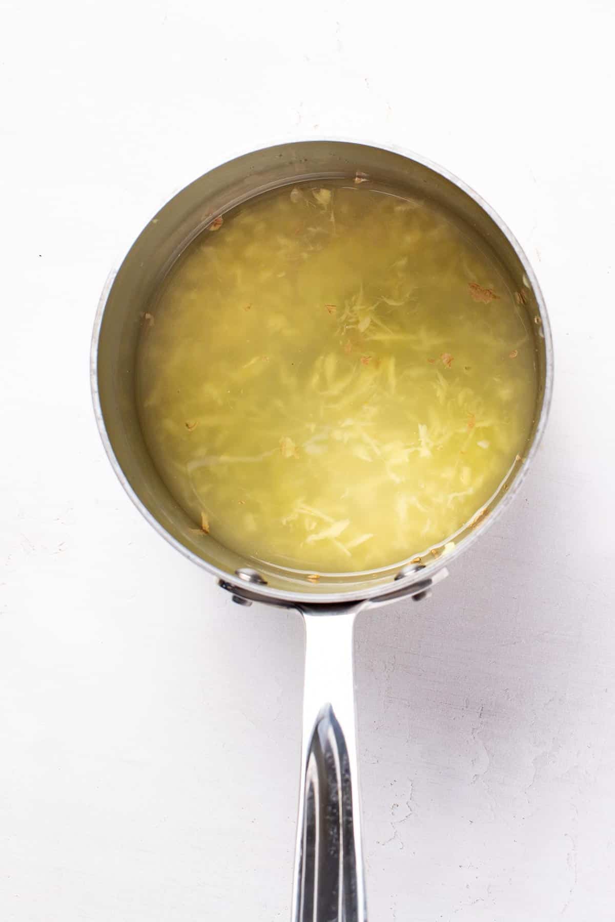 Fresh grated ginger in a small pot with water.