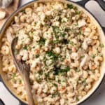 A creamy chicken pot pie pasta in a large cast iron pot with a wood spoon stirring the pasta.