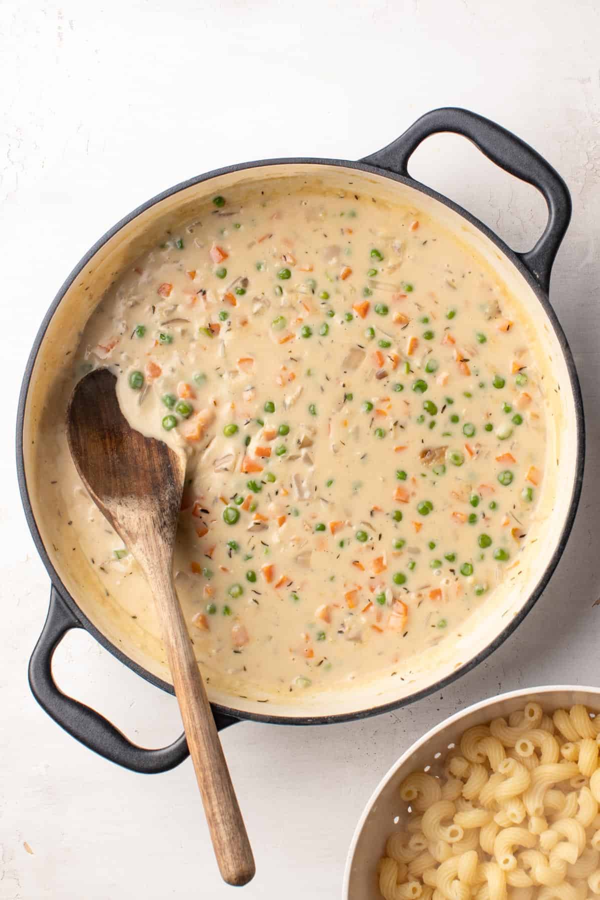 A wood spoon stirring a creamy sauce with frozen veggies and spices.