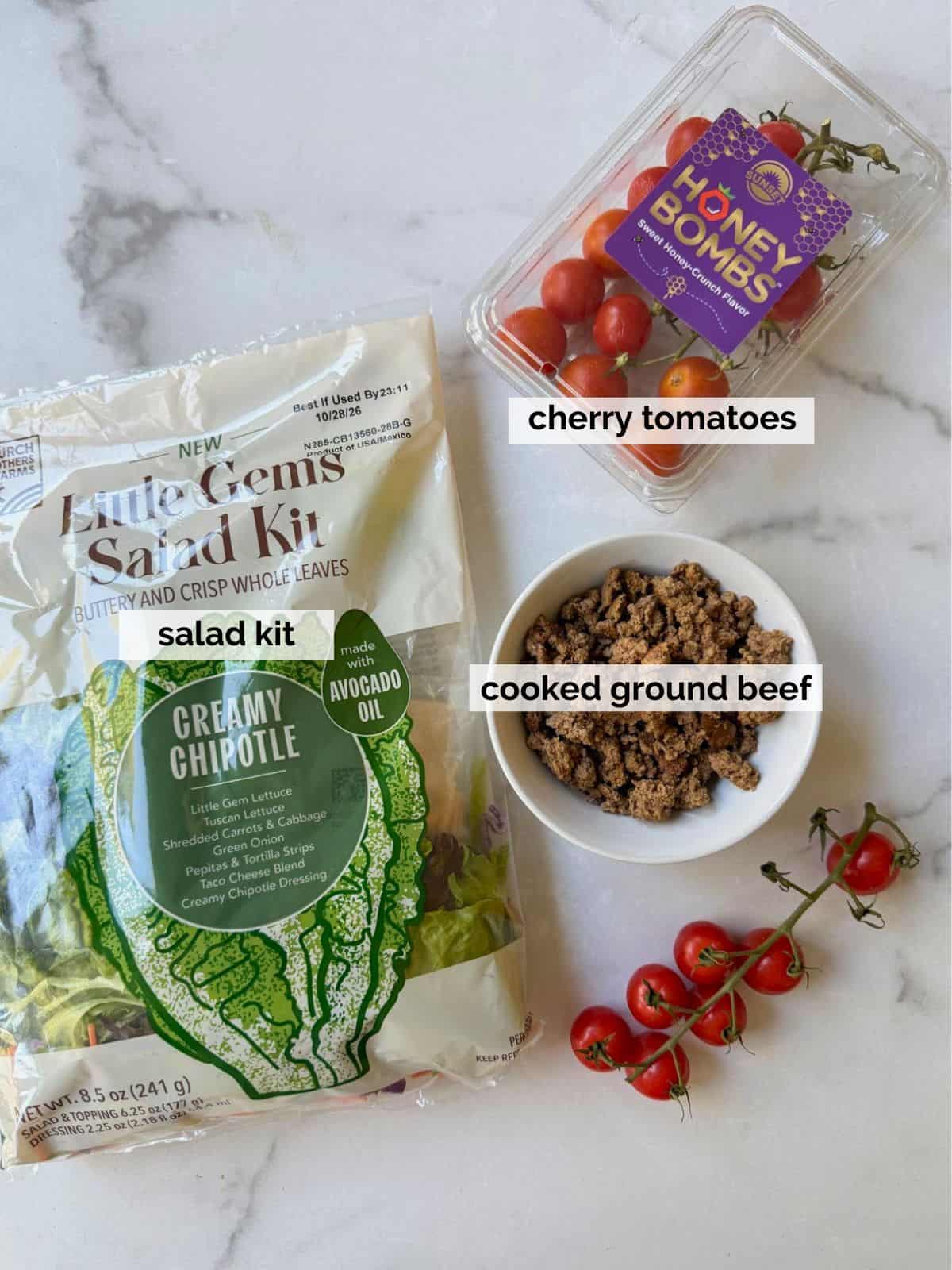 A salad kit, cooked ground beef, and tomatoes on a white background.