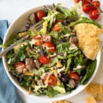 A salad with ground beef, tortilla chips, tomatoes, and chipotle dressing drizzled on top.