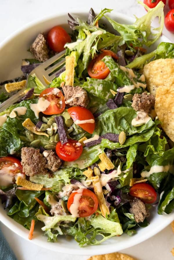A salad with ground beef, tortilla chips, tomatoes, and chipotle dressing drizzled on top.