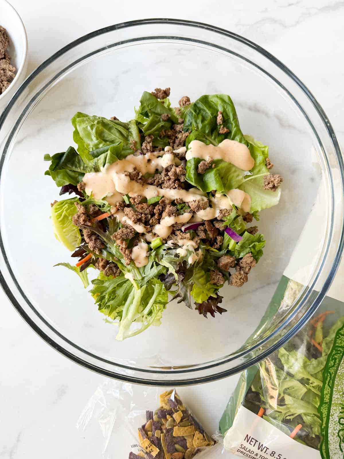 Mixing salad greens with ground beef and chipotle dressing.