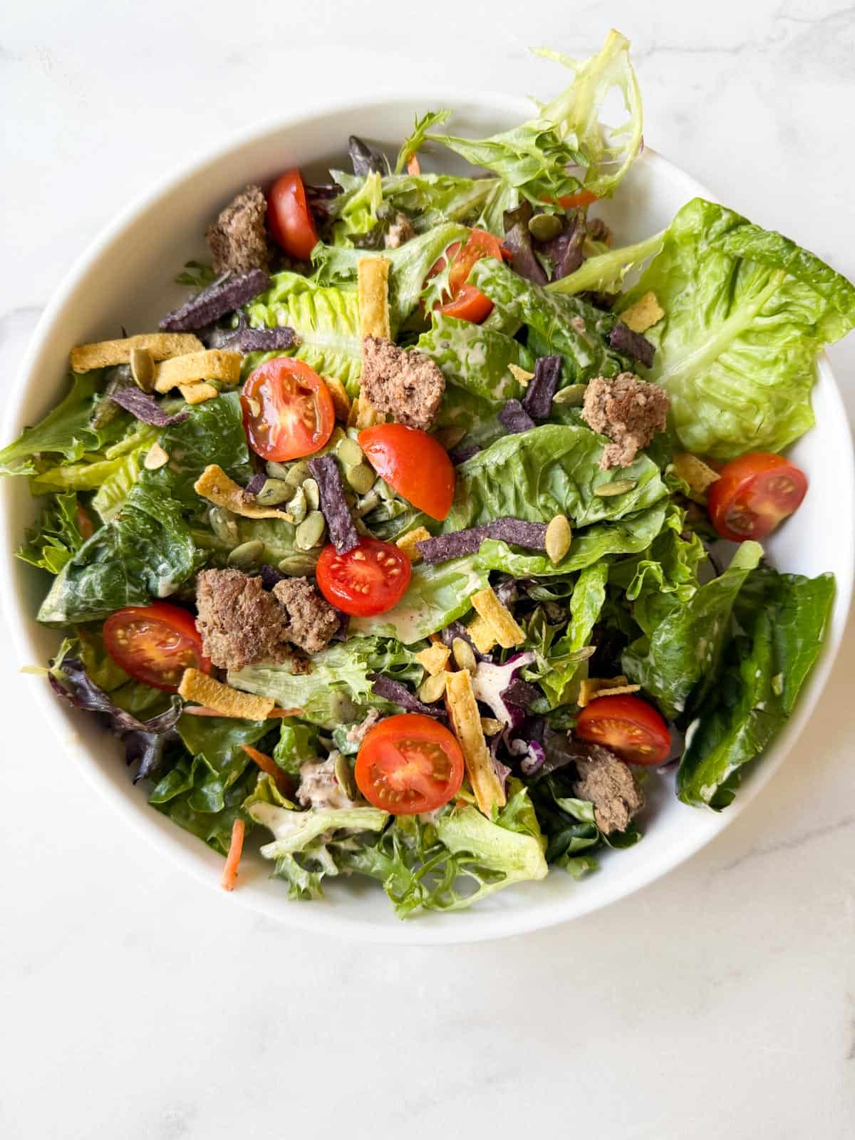 Salad with ground beef and tomatoes in a white bowl.