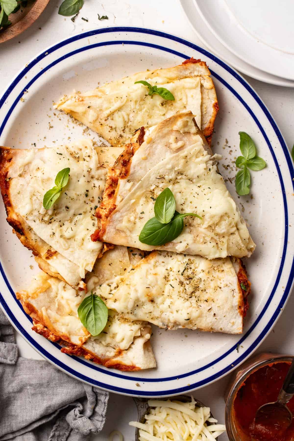 Pizza quesadillas layered on top of each other on a blue and white plate with fresh basil.
