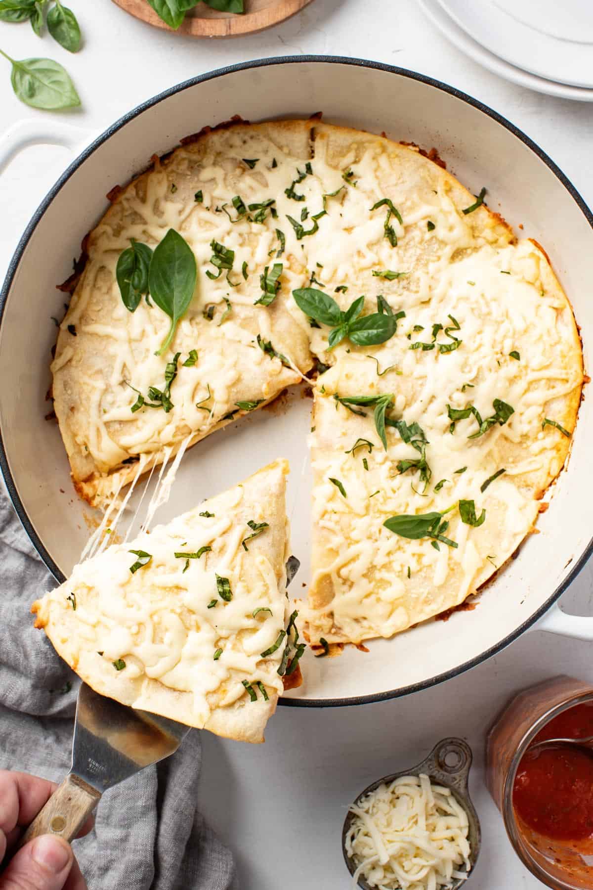 Pulling a pizzilla slice out of the pan with melty cheese and fresh basil sprinkled on top.