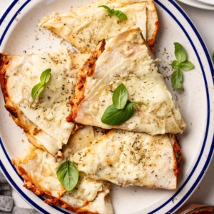 Pizza quesadilla slices layered on top of each other on a plate with fresh basil on top.