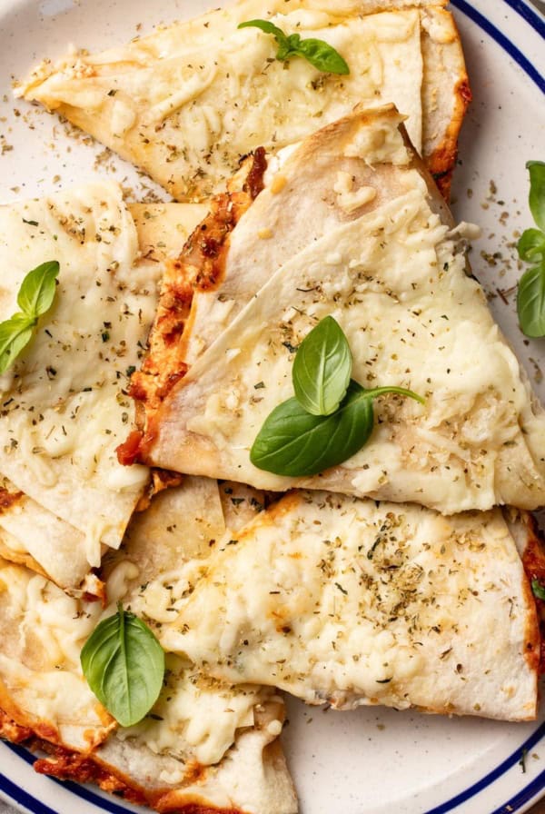 Pizza quesadilla slices layered on top of each other on a plate with fresh basil on top.