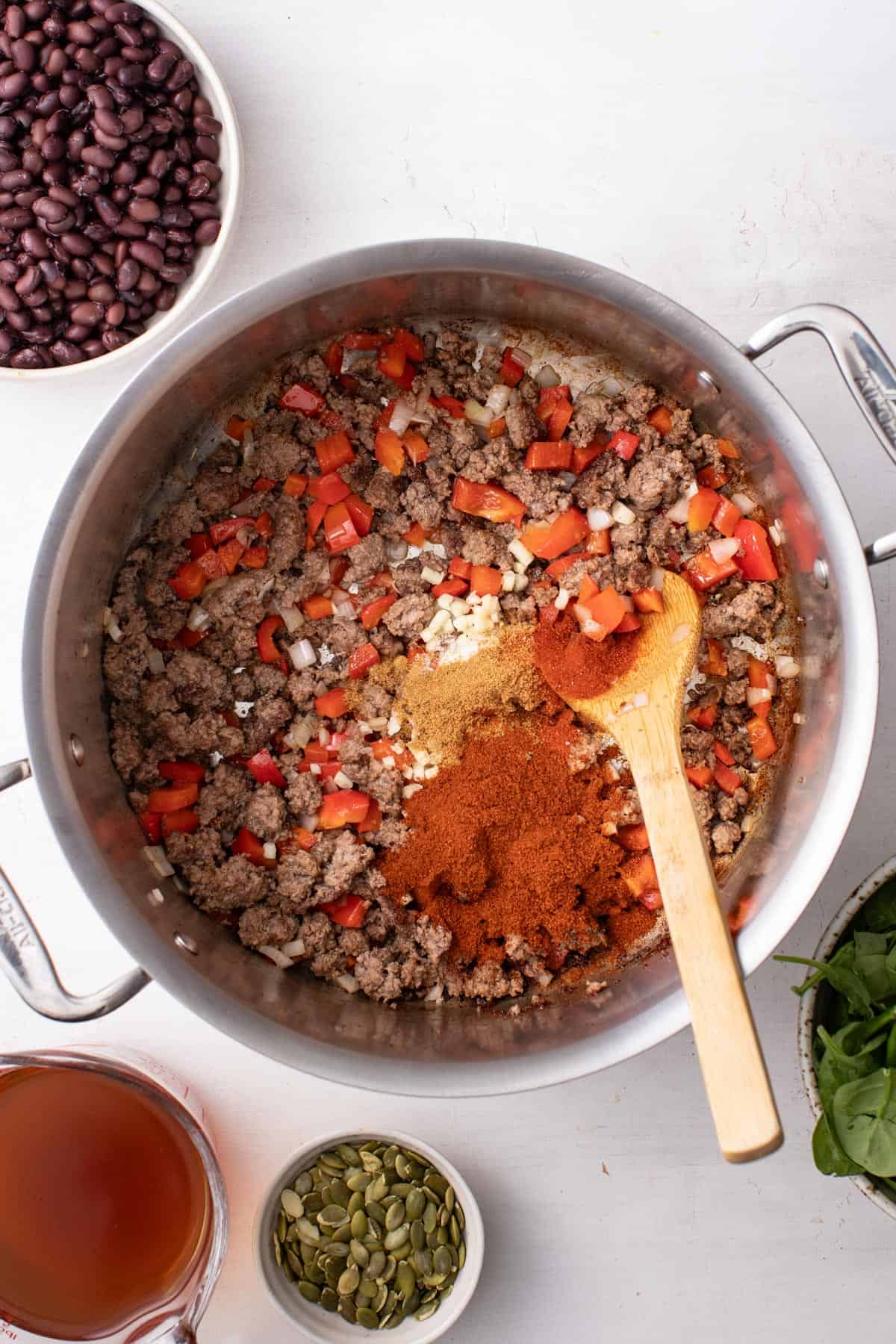 An overhead shot showing stirring in vegetables and tomatoes with spices into the ground beef, in a large soup pot.