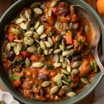 A bowl of pumpkin chili with ground beef and pumpkin seeds on top.