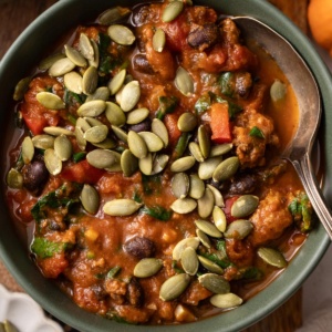 A bowl of pumpkin chili with ground beef and pumpkin seeds on top.