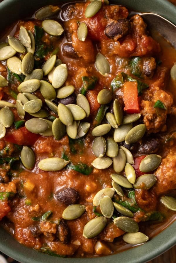 A bowl of pumpkin chili with ground beef and pumpkin seeds on top.